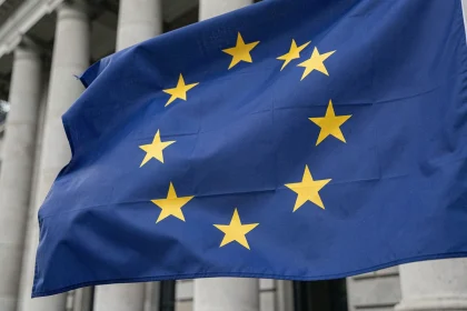 Gros plan sur les douze étoiles dorées du drapeau européen en cercle sur fond bleu cobalt, devant un bâtiment officiel